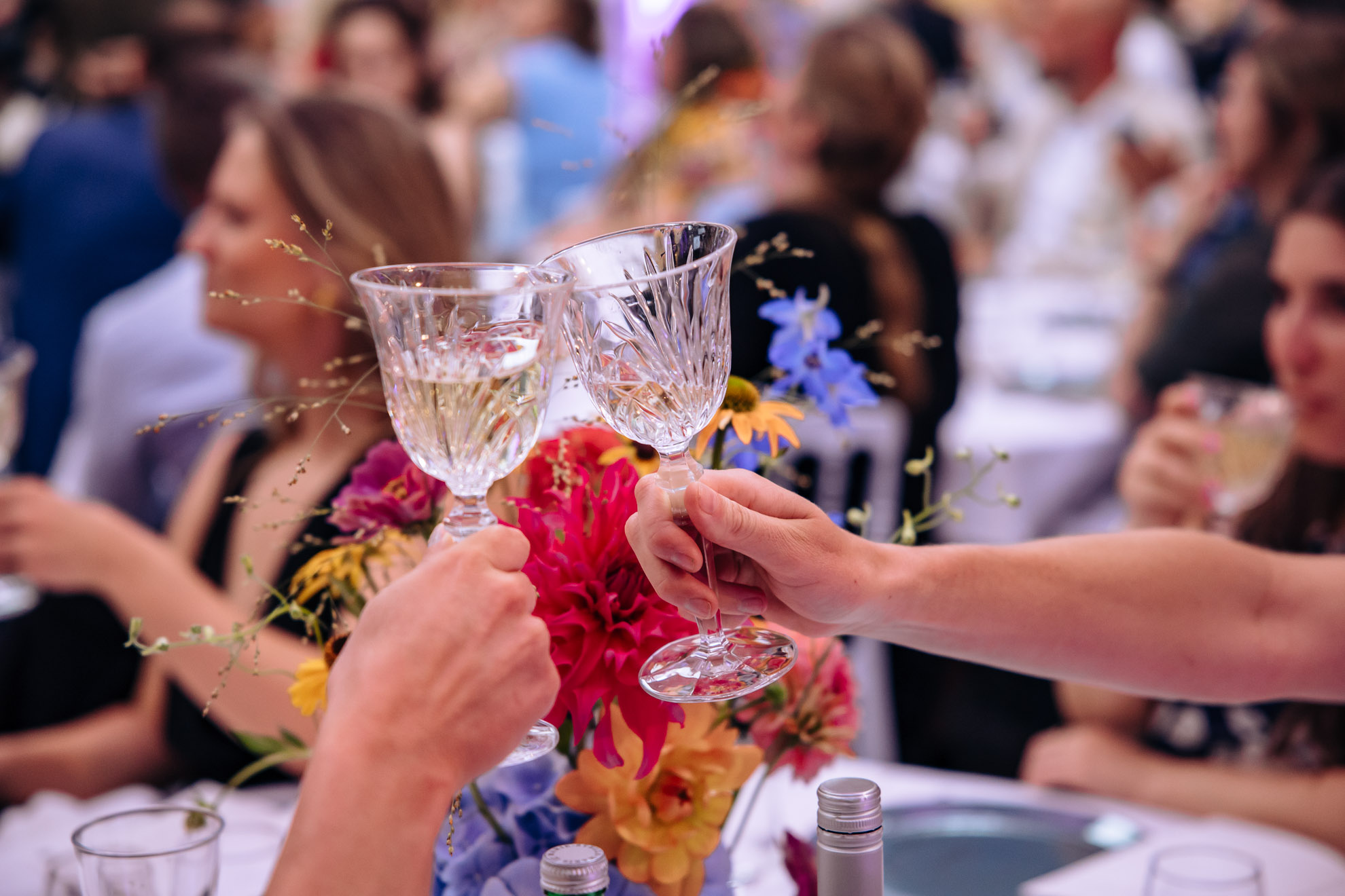 Twee glazen witte wijn die tegen elkaar klinken boven een boeket veldbloemen